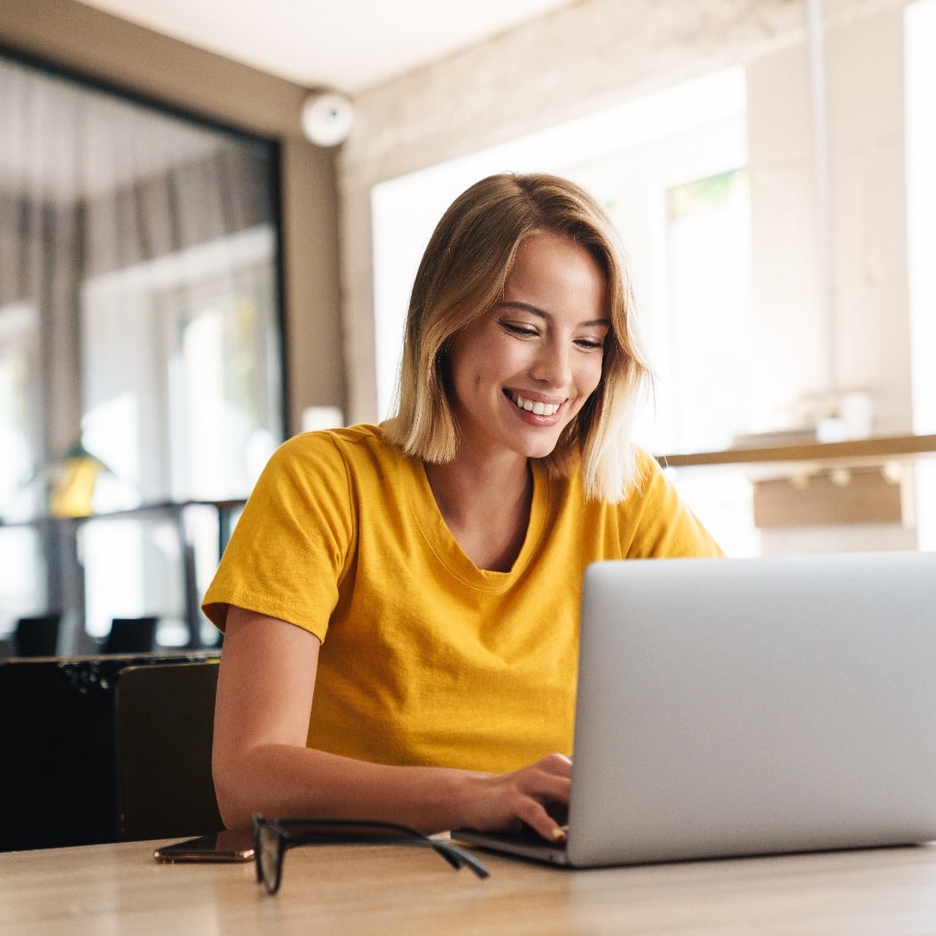 Photo of joyful nice woman using laptop and smiling while sitting